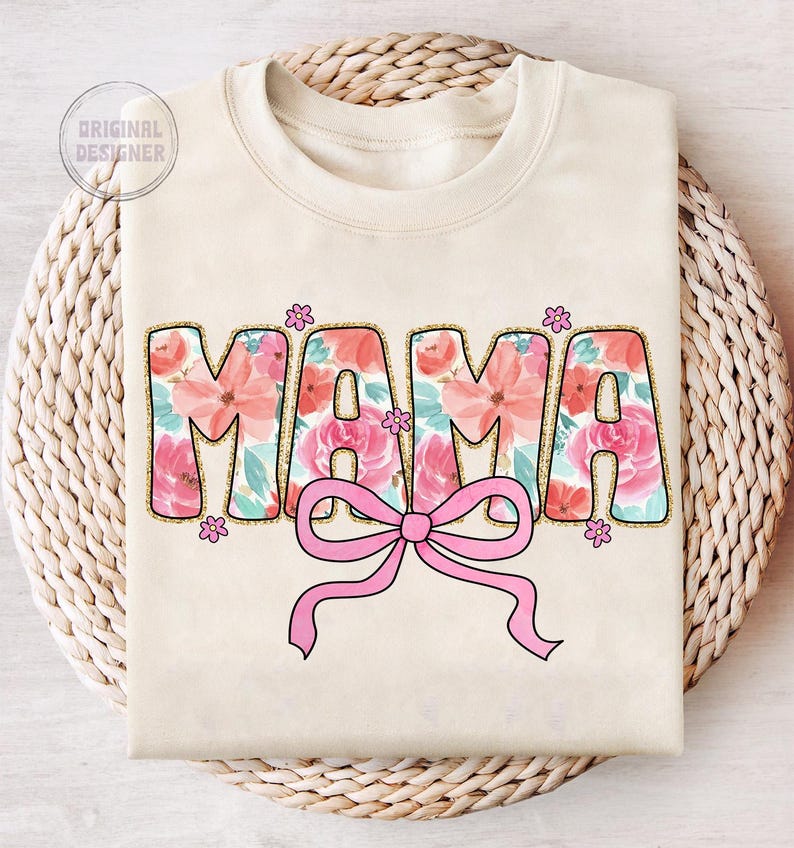 May include: A beige sweatshirt with the word "MAMA" in pink and white floral letters with a pink bow in the center.