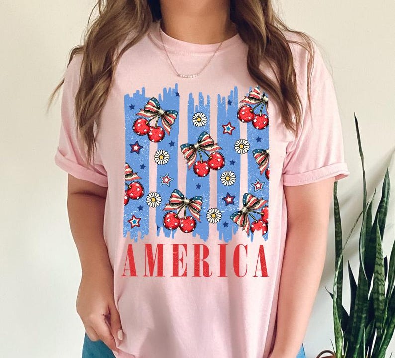 May include: Pink t-shirt with a blue and red graphic of cherries and stars with the word "AMERICA" printed below.