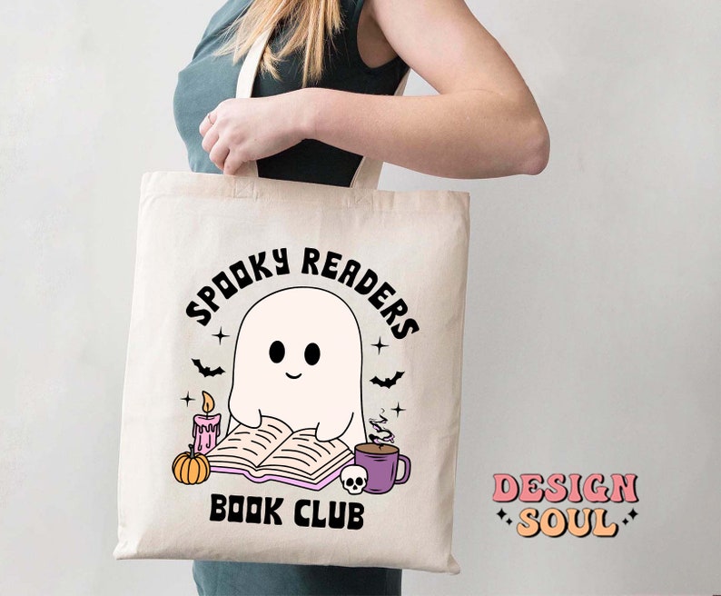 May include: A white tote bag with a black and white illustration of a ghost reading a book. The text on the bag reads "Spooky Readers Book Club".