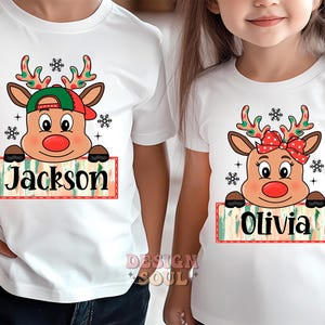 May include: Two white t-shirts with a Christmas reindeer design. The reindeer is wearing a red and green hat and has a red nose. The shirts have the names "Jackson" and "Olivia" printed on them.