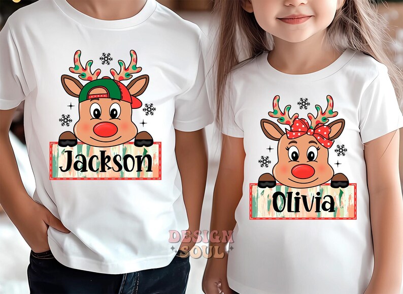 May include: Two white t-shirts with a Christmas reindeer design. The reindeer is wearing a red and green hat and has a red nose. The shirts have the names "Jackson" and "Olivia" printed on them.
