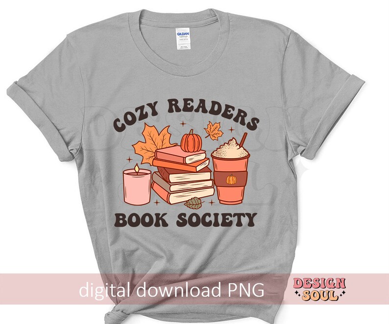 May include: Gray t-shirt with a graphic design of a stack of books, a candle, a pumpkin, and a cup of coffee. The text "Cozy Readers Book Society" is printed on the shirt.