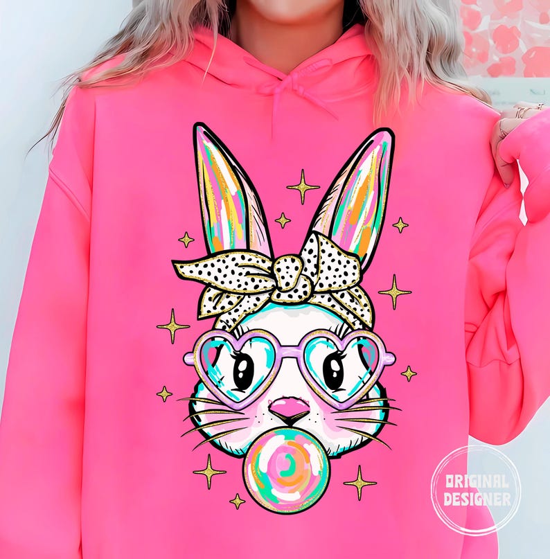 May include: Pink hoodie with a graphic of a cartoon bunny wearing heart-shaped sunglasses and a polka dot headband. The bunny is holding a colorful lollipop.