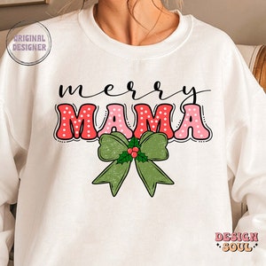 May include: White sweatshirt with a red and pink "merry mama" graphic with white polka dots. A green bow with holly and red berries is below the text.