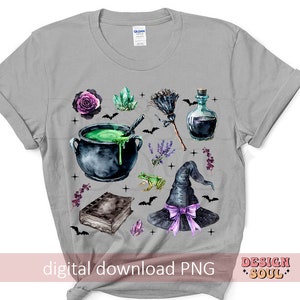 May include: A gray t-shirt with a watercolor design of a witch's hat, cauldron, potion bottle, frog, and other magical elements. The design is in shades of purple, green, and black.