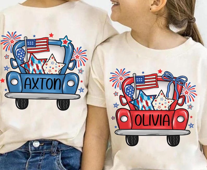 May include: Two cream-colored t-shirts with matching patriotic designs. One shirt features a blue truck with the name "AXTON" and the other a red truck with the name "OLIVIA". Both designs include an American flag, stars, and fireworks.