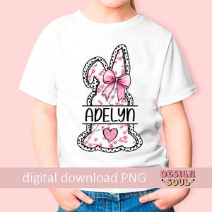Pu&ograve; includere: Una maglietta bianca con un design di coniglio rosa. Il coniglio &egrave; decorato con fiori rosa e un fiocco rosa. Il nome "Adelyn" &egrave; scritto in lettere nere sotto il coniglio.