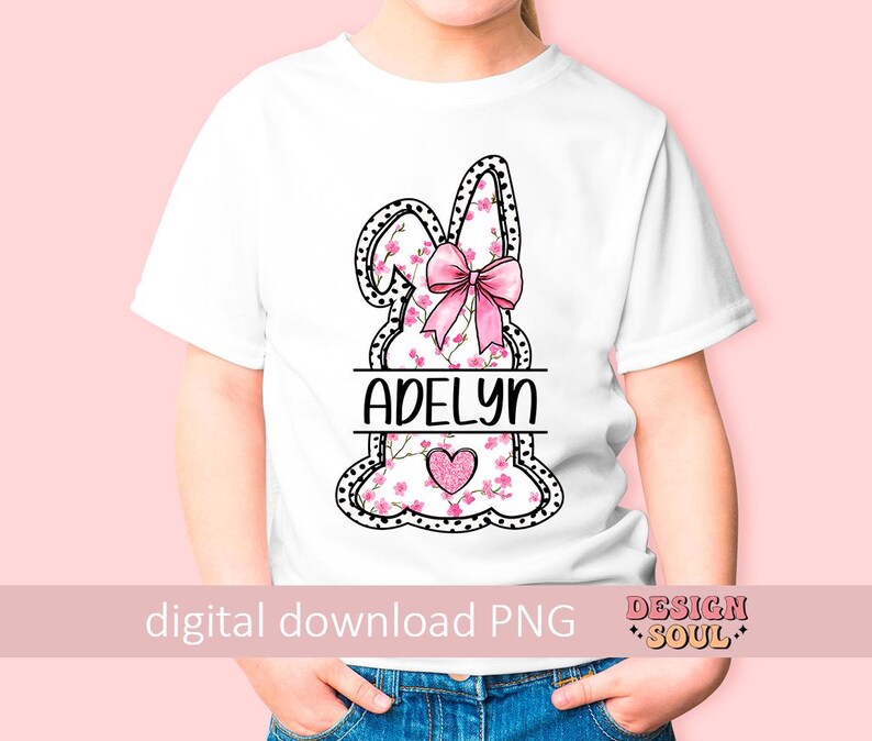 Pu&ograve; includere: Una maglietta bianca con un design di coniglio rosa. Il coniglio &egrave; decorato con fiori rosa e un fiocco rosa. Il nome "Adelyn" &egrave; scritto in lettere nere sotto il coniglio.