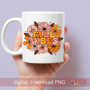 May include: White ceramic mug featuring a design of orange and pink flowers with the text "Fall Vibes" in a retro font.