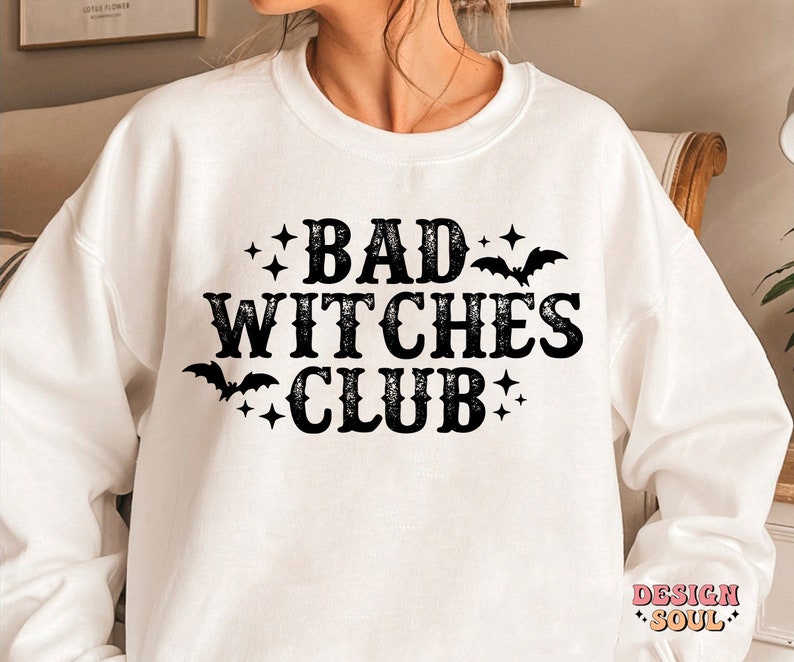 May include: White sweatshirt with the text "BAD WITCHES CLUB" in black, decorated with bats and stars. A casual, comfortable top for Halloween or everyday wear.