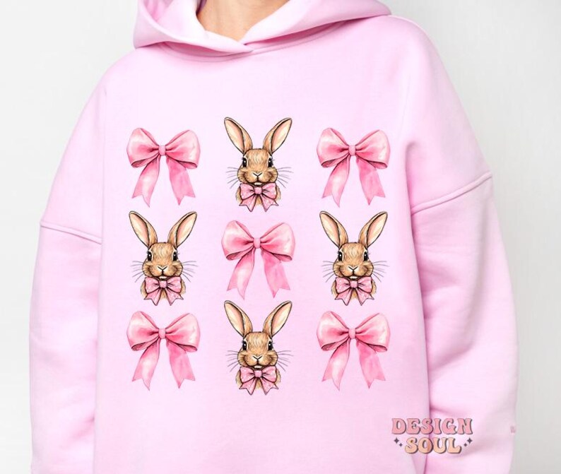 May include: Pink hoodie with a repeating pattern of brown bunnies wearing pink bows. The hoodie has a large hood and long sleeves.