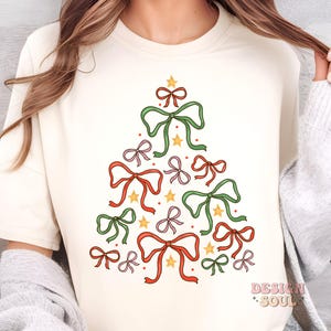 May include: A white t-shirt featuring a Christmas tree design made up of bows in red, green and pink. The bows are tied with gold ribbon and have gold stars in the centre.
