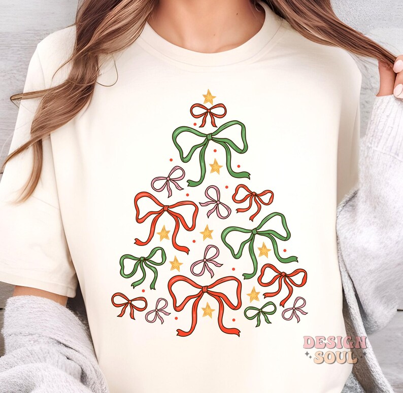 May include: A white t-shirt featuring a Christmas tree design made up of bows in red, green and pink. The bows are tied with gold ribbon and have gold stars in the centre.
