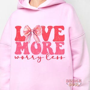 May include: Pink hoodie with a pink bow and the text "LOVE MORE worry less" in red and pink.
