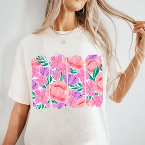May include: A white t-shirt with a floral print design. The print features pink, purple, and green flowers.