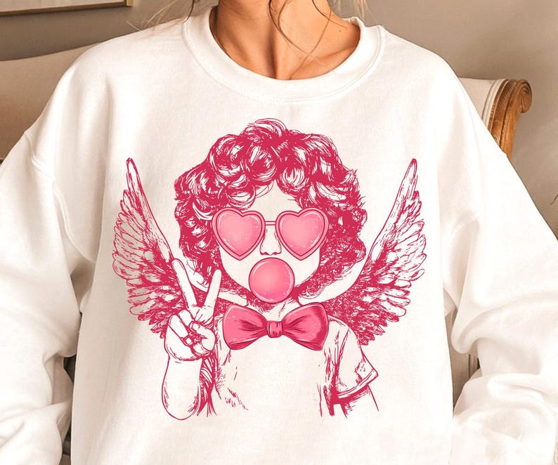 May include: White sweatshirt featuring a pink graphic of a cherub with angel wings wearing heart-shaped sunglasses and blowing a bubble. The cherub is giving the peace sign.