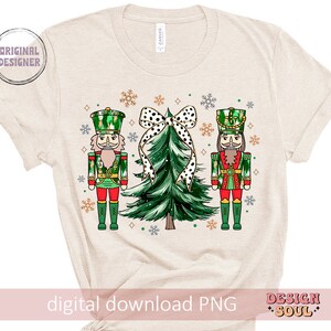 May include: Beige t-shirt with a festive Christmas design. The design features two nutcrackers in green and red uniforms, a green Christmas tree with a black and white polka dot bow, and snowflakes. The text "digital download PNG" is at the bottom.