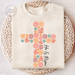 May include: A cream-colored sweatshirt with a floral cross design and the text "He is Risen".