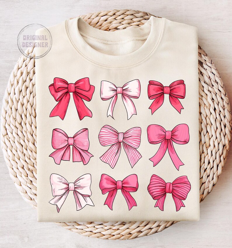 May include: A beige sweatshirt with a design of nine pink bows in different styles. The bows are arranged in three rows of three.