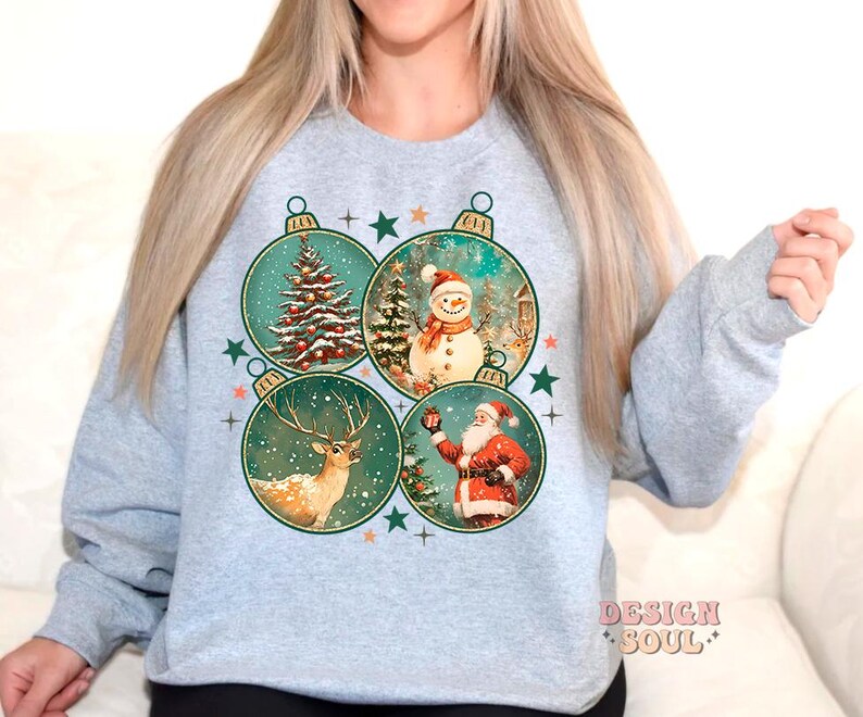 May include: A grey sweatshirt with a Christmas design featuring four baubles. Each bauble has a different image: a snowman, a deer, a Christmas tree, and Santa Claus. The baubles are surrounded by stars and snowflakes.