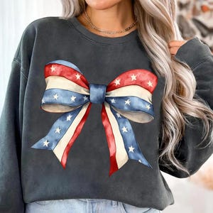 K&ouml;nnte beinhalten: Ein dunkelgraues Sweatshirt mit einer gro&szlig;en rot-wei&szlig;-blauen Schleife mit wei&szlig;en Sternen darauf.