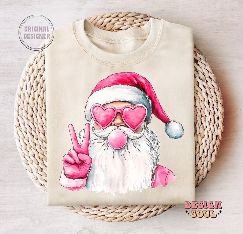 May include: A beige sweatshirt featuring a pink and white illustration of Santa Claus wearing heart-shaped sunglasses and blowing a bubble. Santa is giving the peace sign with his right hand.