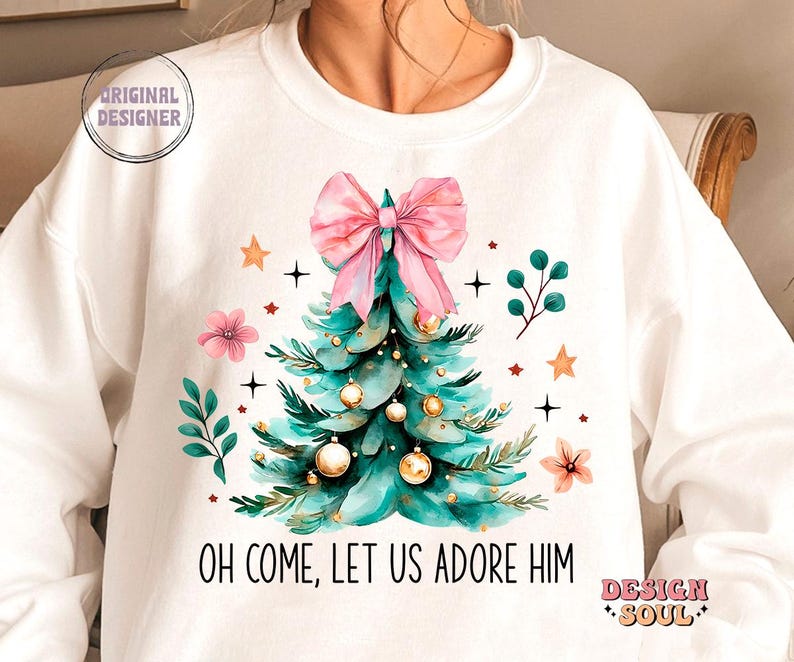 May include: White sweatshirt with a green Christmas tree with pink bow and gold ornaments. The text "Oh come, let us adore Him" is printed below the tree.