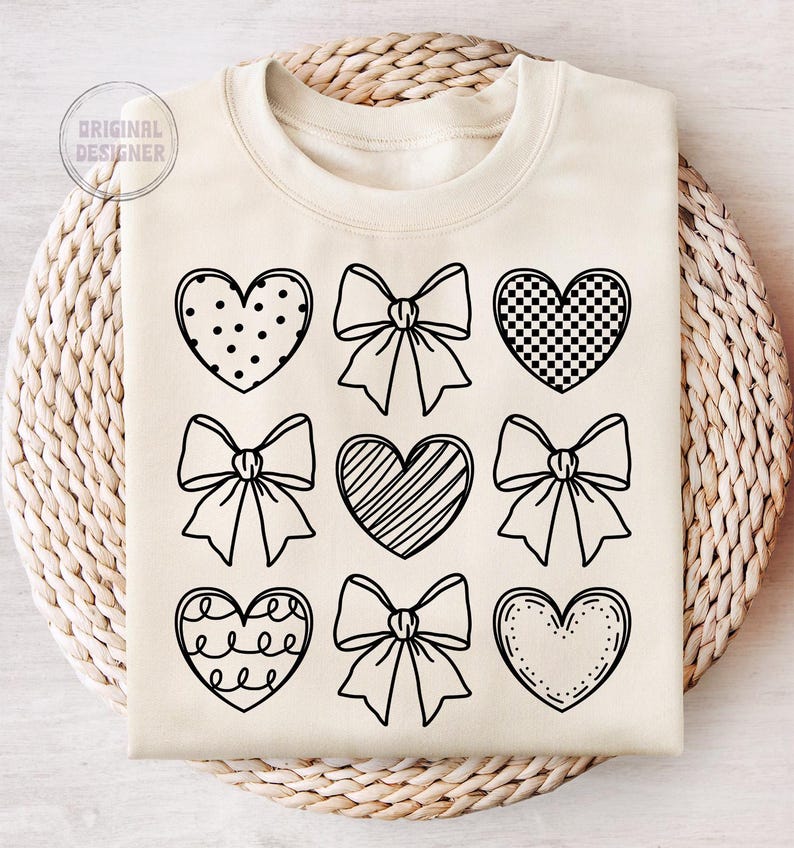 May include: A cream-colored sweatshirt with a black outline of various hearts and bows. The hearts have different patterns, including polka dots, checkered, and stripes.