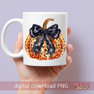 May include: A white ceramic mug with a black and orange leopard print pumpkin with a black bow. The pumpkin is centered on the mug.