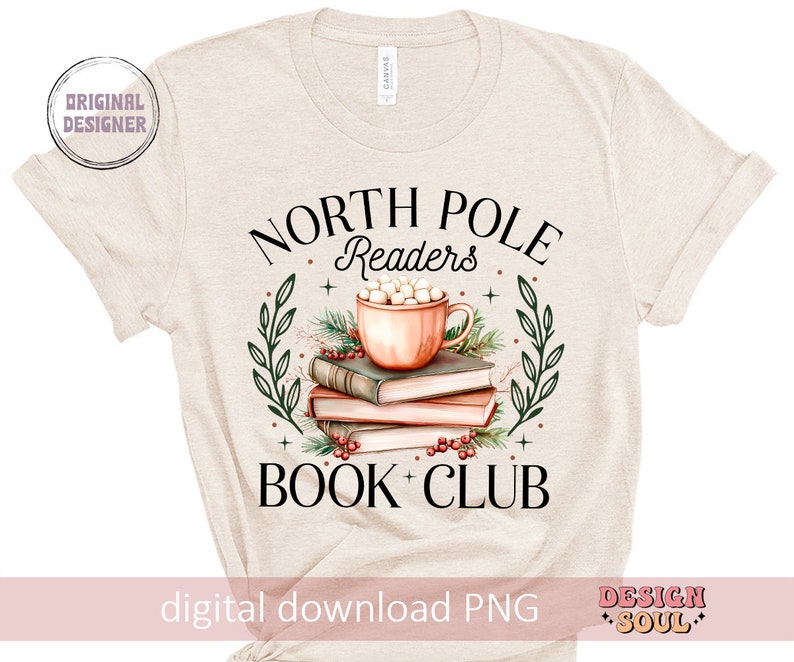May include: A beige t-shirt with the text "North Pole Readers Book Club" in black. The design features a mug of hot chocolate with marshmallows, surrounded by books and greenery.