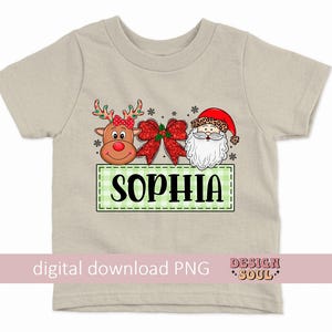 May include: A beige t-shirt with a green and white checkered box with the name "Sophia" in black text. The box is decorated with a red and white bow, a cartoon reindeer with a red nose, and a cartoon Santa Claus with a red hat.