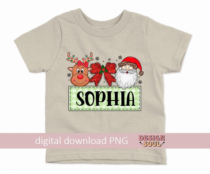 May include: A beige t-shirt with a green and white checkered box with the name "Sophia" in black text. The box is decorated with a red and white bow, a cartoon reindeer with a red nose, and a cartoon Santa Claus with a red hat.