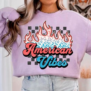 May include: A lavender sweatshirt with a graphic design of flames with a leopard print pattern. The text "American Vibes" is in a retro font.