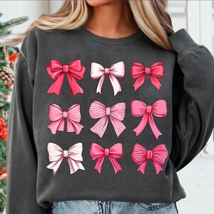 May include: A charcoal grey sweatshirt with a pattern of nine pink and white bows. The bows are arranged in a grid pattern.