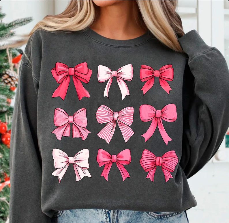 May include: A charcoal grey sweatshirt with a pattern of nine pink and white bows. The bows are arranged in a grid pattern.