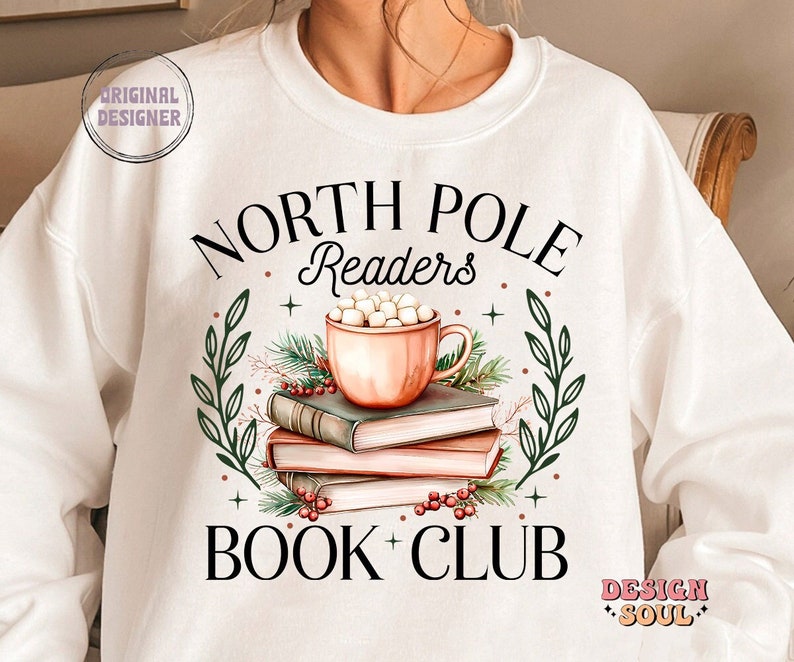 May include: White sweatshirt with a black graphic design that says "North Pole Readers Book Club". The graphic features a mug of hot chocolate with marshmallows, a stack of books, and holly berries.