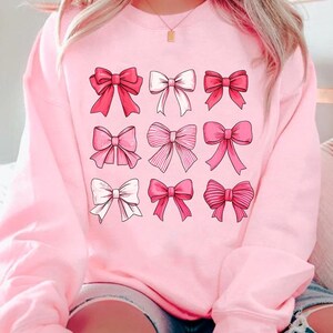 May include: Pink sweatshirt with a graphic of nine pink bows of different styles.