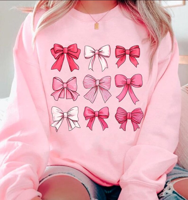 May include: Pink sweatshirt with a graphic of nine pink bows of different styles.