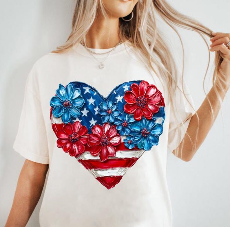 May include: A white t-shirt with a red, white, and blue heart-shaped design. The heart is made up of flowers and the American flag.