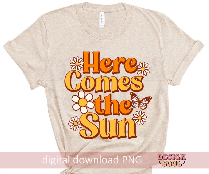 May include: A beige t-shirt with a graphic design that says "Here Comes the Sun" in orange and yellow letters with a butterfly and flowers in orange, yellow, and white.