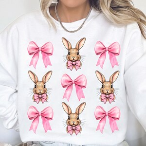 May include: White sweatshirt with a repeated pattern of pink bows and brown bunnies wearing pink bows.