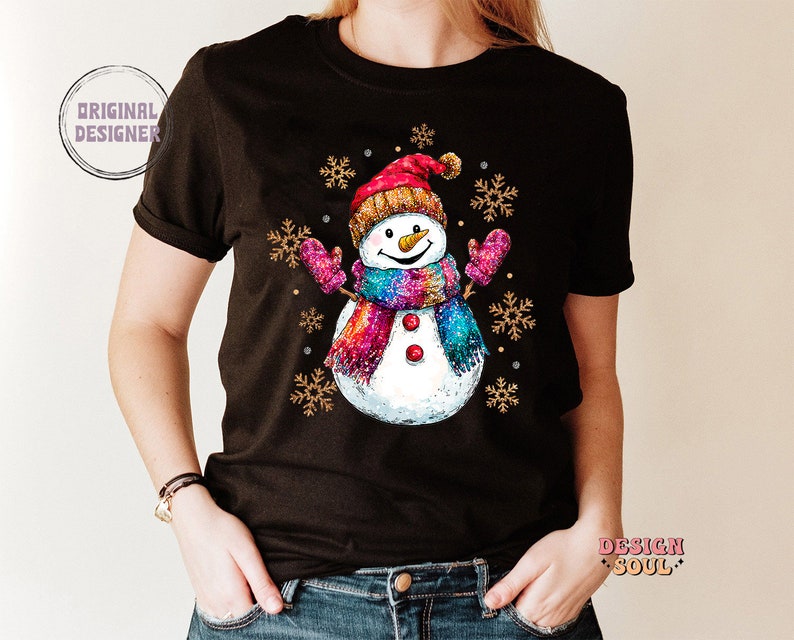 May include: Black t-shirt with a colorful snowman wearing a red hat and a pink scarf. The snowman is surrounded by snowflakes.