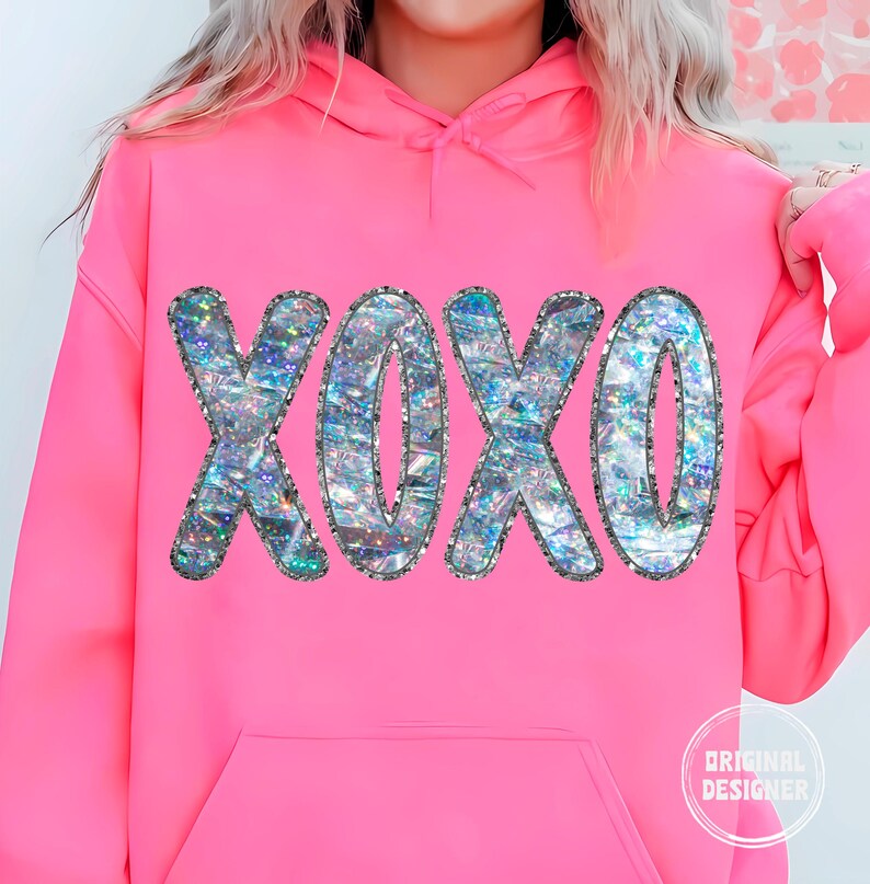 May include: A pink hoodie with a large iridescent glitter XOXO graphic on the front. The hoodie has a drawstring hood and a kangaroo pocket.