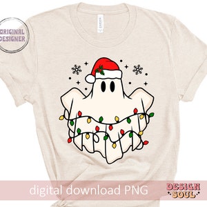 May include: A white ghost wearing a red Santa hat with green holly and a string of colorful Christmas lights around it. The ghost is on a beige t-shirt.