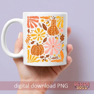 May include: A white ceramic mug with a fall-themed design. The design features orange, yellow, and pink flowers, leaves, and pumpkins with a leopard print pattern. The text "DESIGN SOUL" is printed on the bottom of the mug.