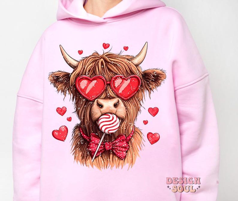 May include: Pink hoodie with a graphic of a Highland cow wearing heart-shaped sunglasses and holding a lollipop. The cow is wearing a red bow tie. The text "DESIGN SOUL" is printed on the bottom right corner of the hoodie.