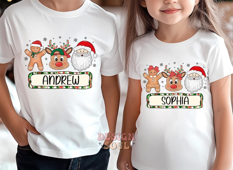 May include: Two white t-shirts with Christmas themed graphics. The first shirt has a gingerbread man, reindeer, and Santa Claus with the name "Andrew" printed below. The second shirt has a gingerbread woman, reindeer, and Santa Claus with the name "Sophia" printed below.
