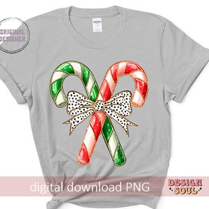 May include: A gray t-shirt with a design of two candy canes tied together with a black and white polka dot bow. The candy canes are red and white with green stripes.