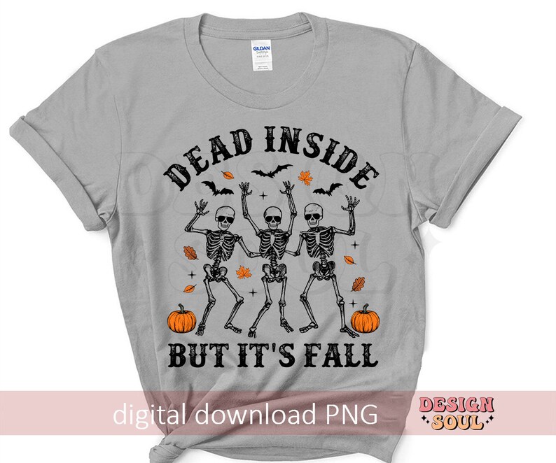 May include: A light gray t-shirt featuring a Halloween design. The graphic includes three dancing skeletons, pumpkins, bats, and fall leaves. The text reads "DEAD INSIDE BUT IT'S FALL".