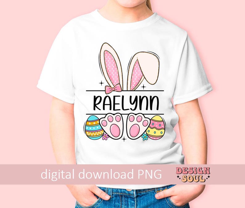 May include: White t-shirt with a pink bunny ears design, a pink bow, and the name "Raelynn" printed on the front. The shirt also features colorful Easter eggs and paw prints.